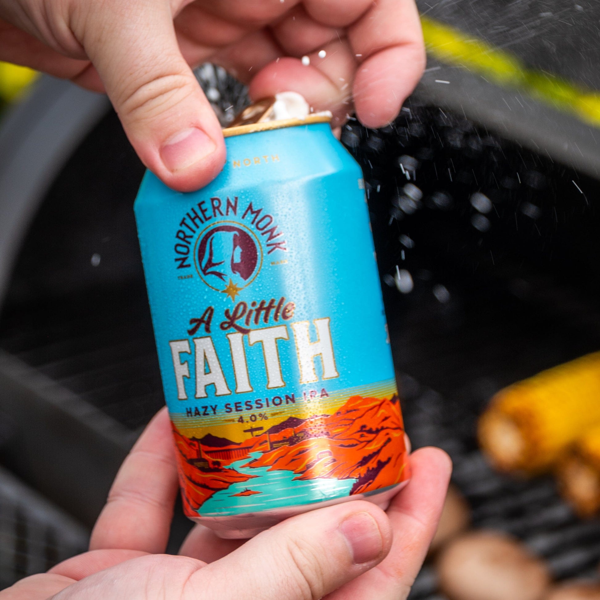 Hand holding a can of 'A Little Faith' beer on a grill
